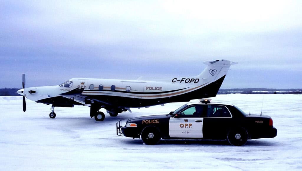 Police aircraft and patrol car on snowy runway.