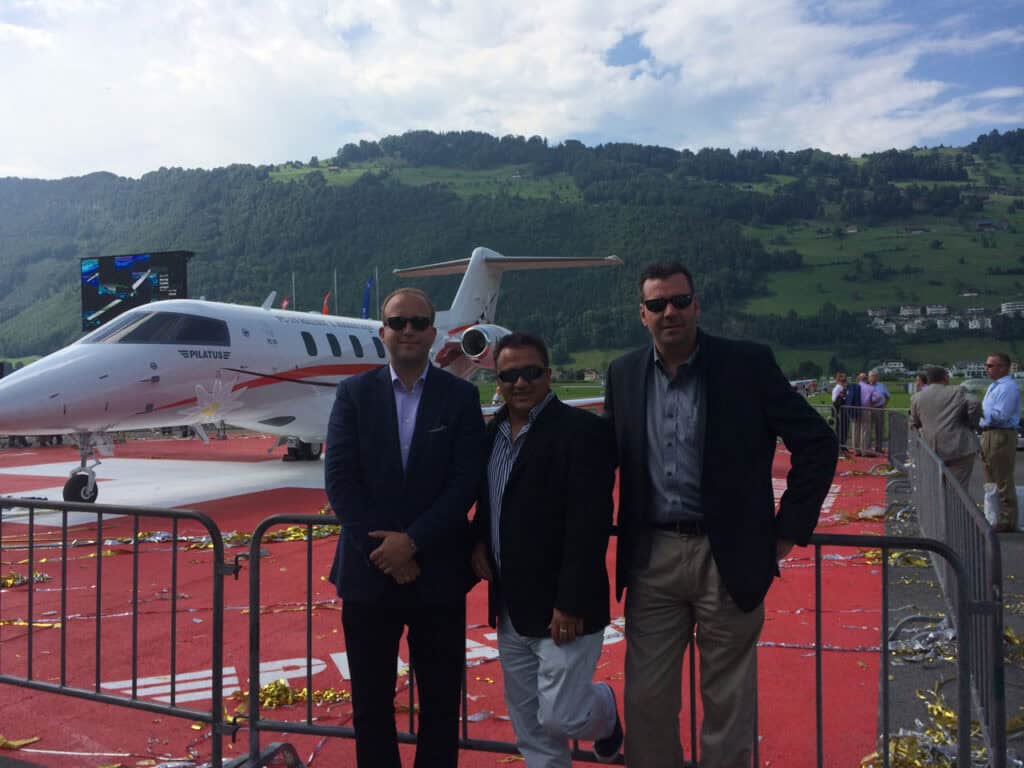 Group of men standing in front of a PC-24 jet at an outdoor event.