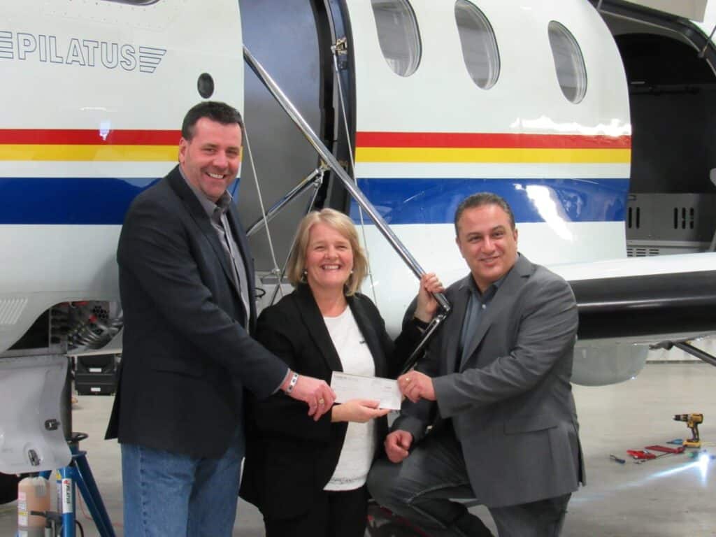 Levaero team presenting check for P.R.O. Kids at aircraft hangar.