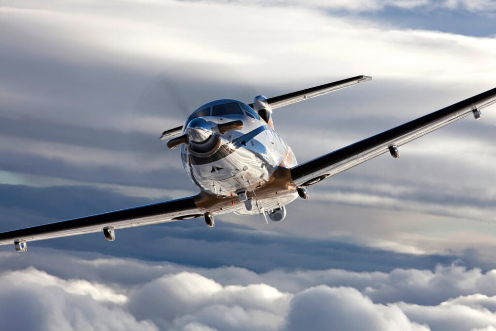 Modern PC-12 aircraft flying through cloudy skies for aerial service.