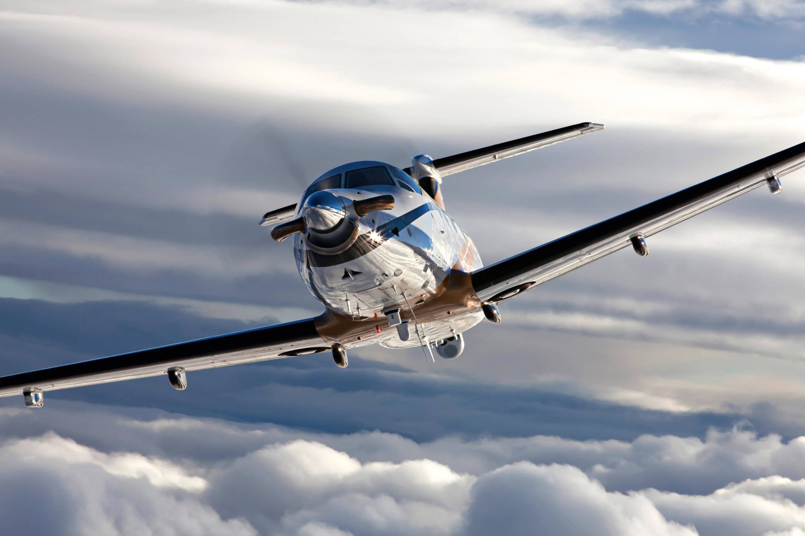 Modern PC-12 aircraft flying through cloudy skies for aerial service.