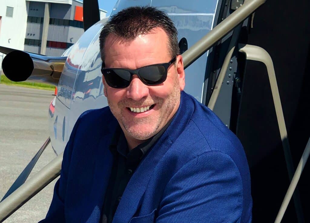 An aviation professional smiling in front of a helicopter at Levaero, showcasing maintenance and rep.