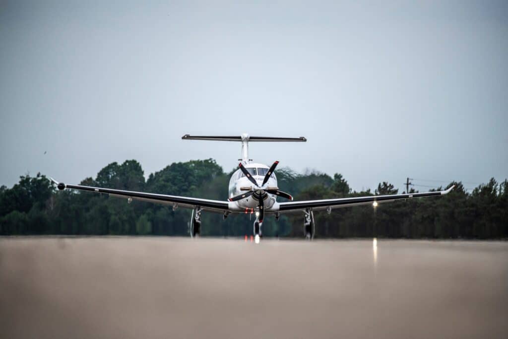 Small private aircraft on runway with trees in background.