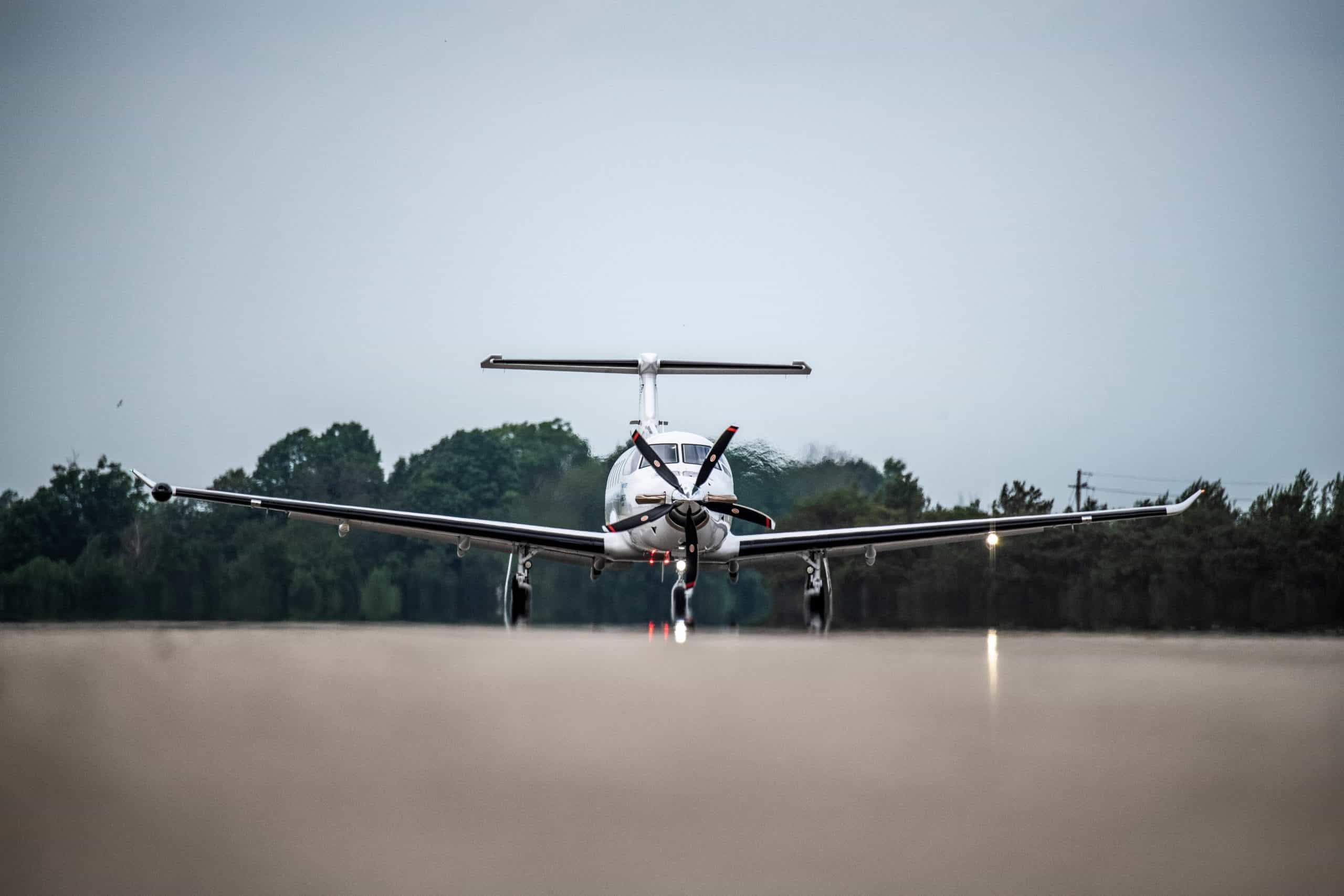 Small private aircraft on runway with trees in background.