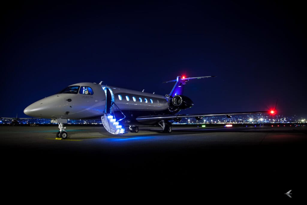 Private jet aircraft parked on the runway at night with illuminated stairs.