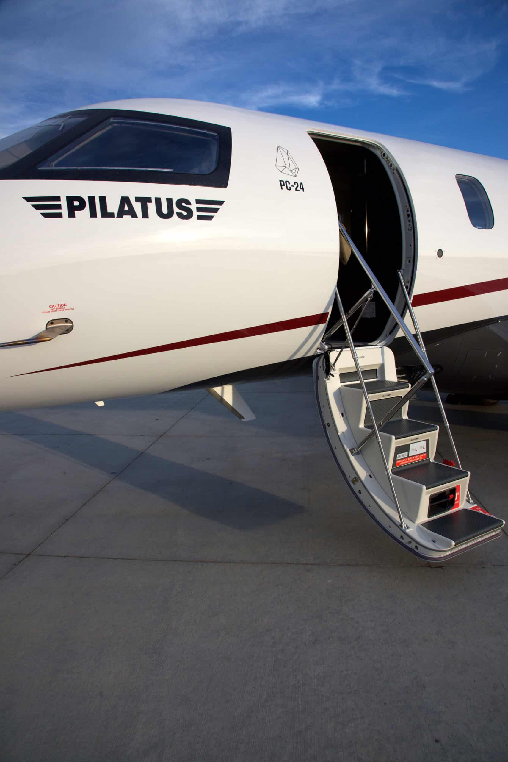 Modern Pilatus private jet with open door and stairs on tarmac.