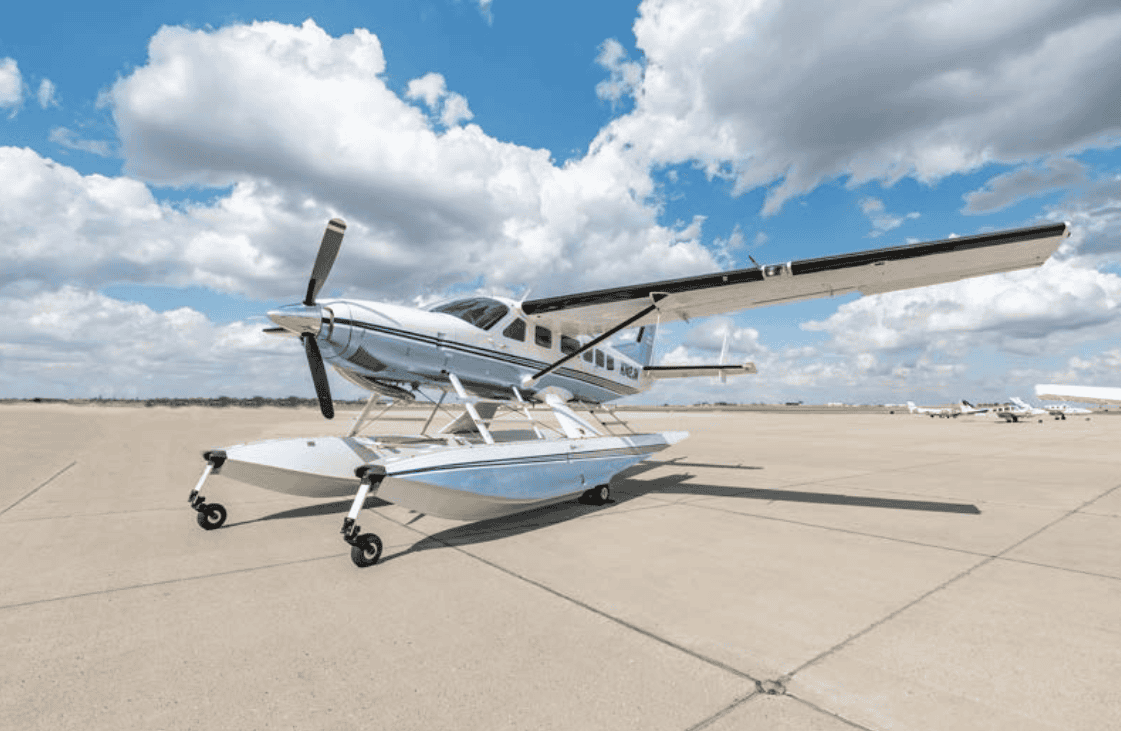 Seaplane parked on airport tarmac with blue sky and clouds in the background.