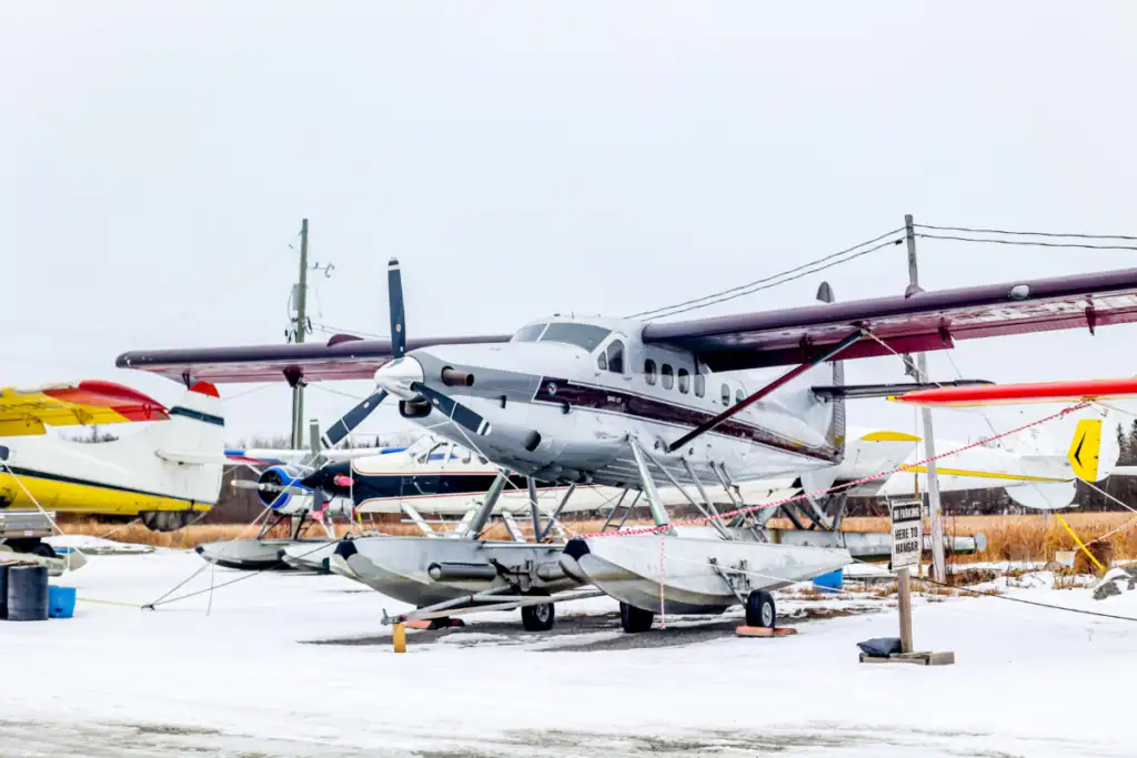 Seaplane parked outdoors on snow-covered ground with other aircraft in the background.