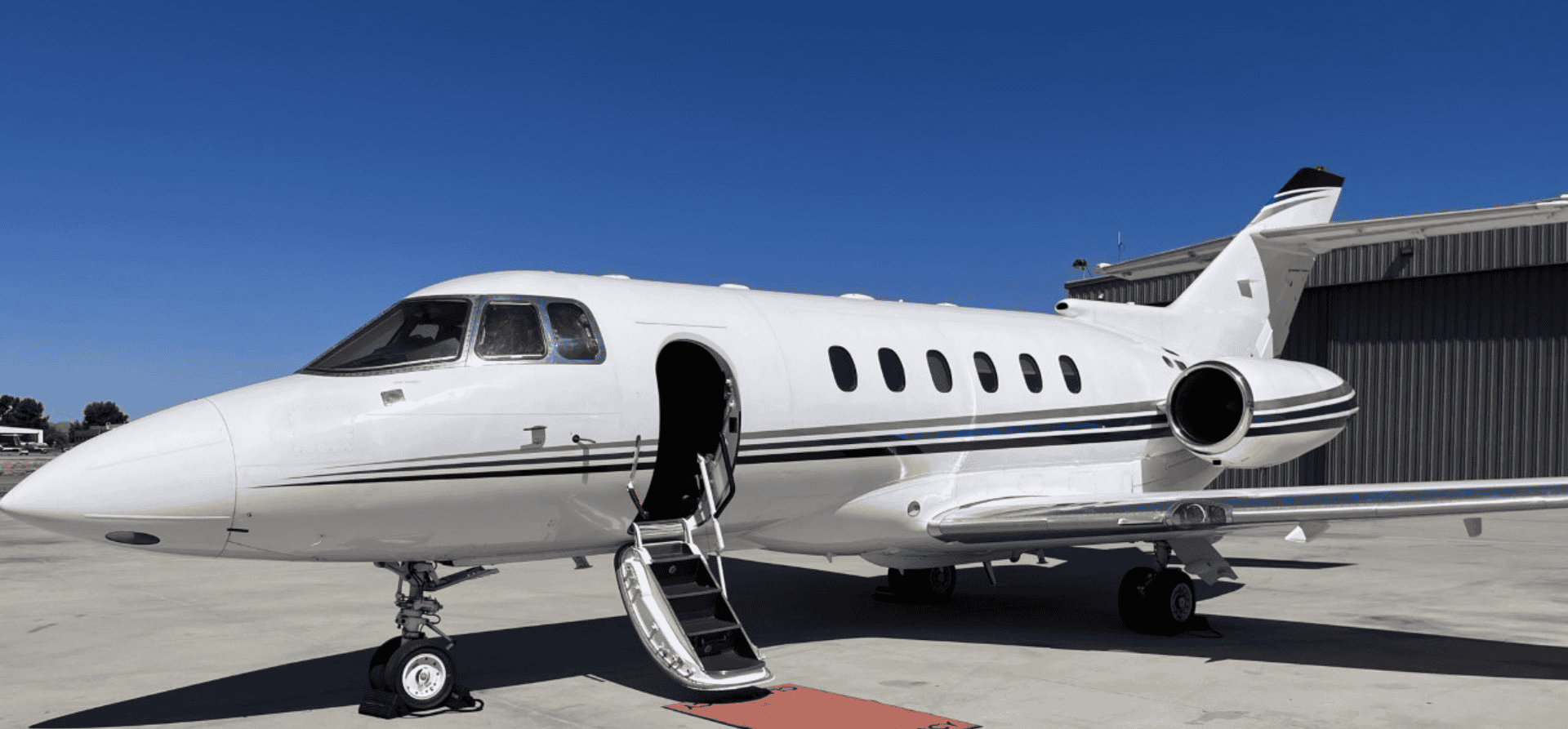 Private jet aircraft on tarmac with open door and stairs.