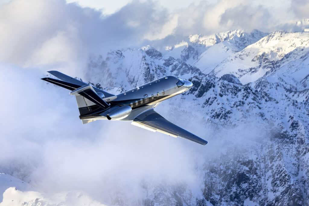 Private jet flying over snow-covered mountains during daytime.