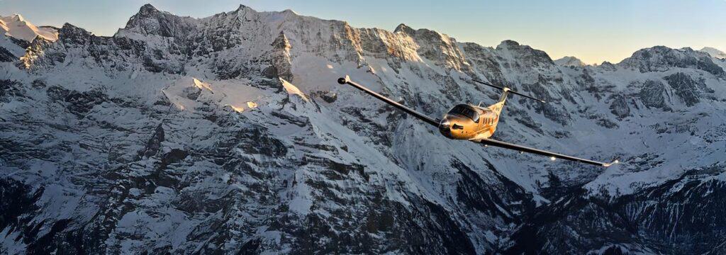 Pilatus PC-12 PRO flying over snow-covered mountain range.