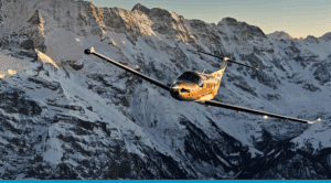 Turboprop aircraft flying over snow-covered mountain range in Canada.