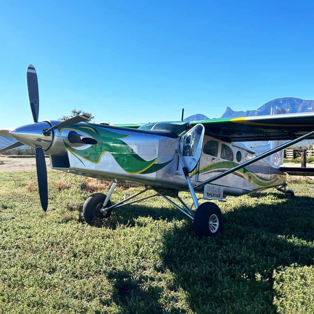 Small aircraft parked on grassy field with mountains in background.
