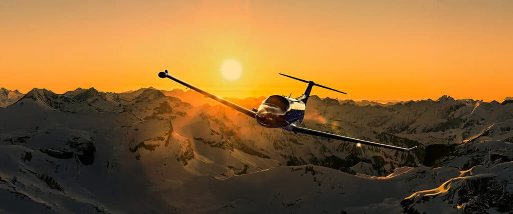 Private jet flying over snowy mountains at sunset.