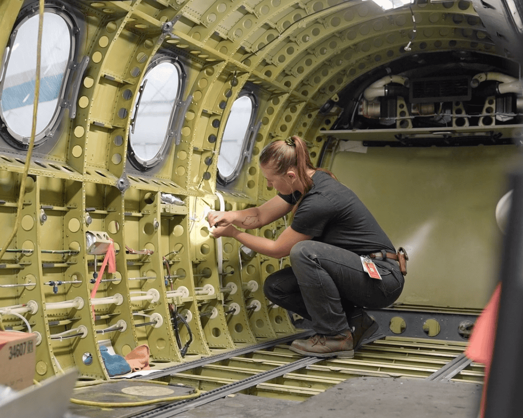 Aircraft Maintenance Engineer inspecting aircraft interior components inside a plane fuselage.