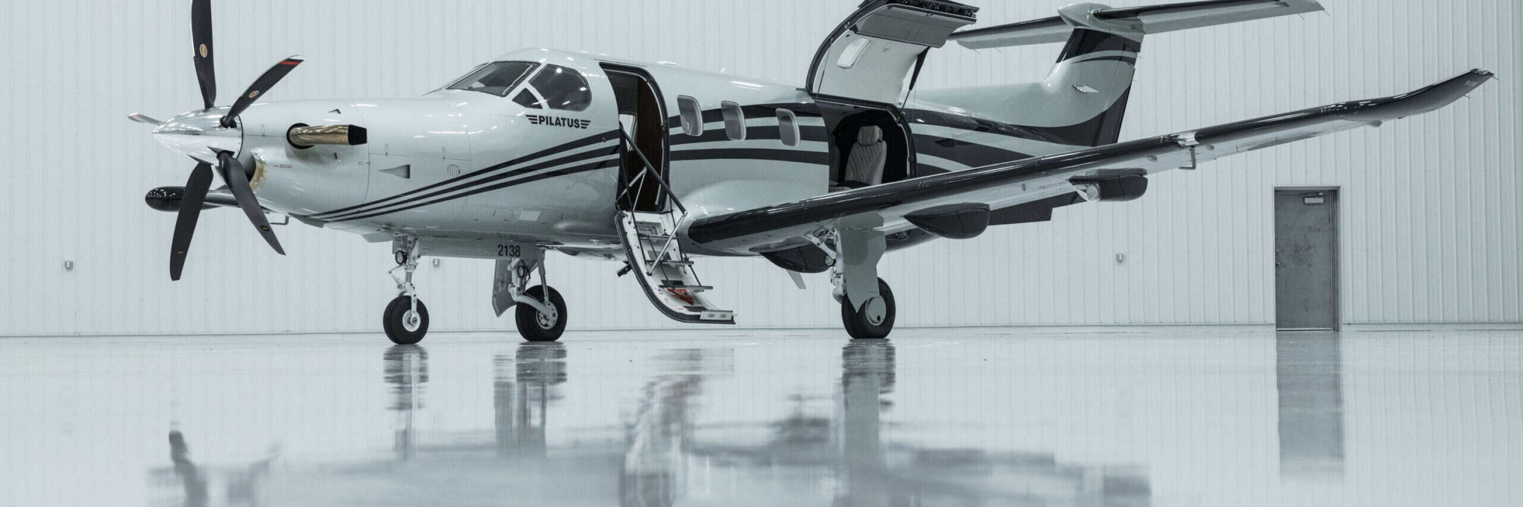 Private jet with open door, ready for passenger boarding in a spacious hangar.