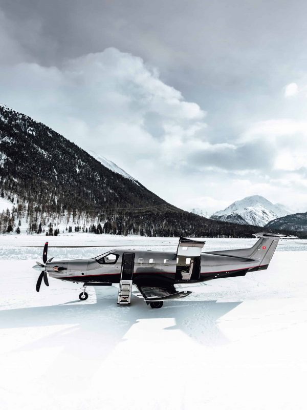 Private jet on snow-covered ground with mountain backdrop.