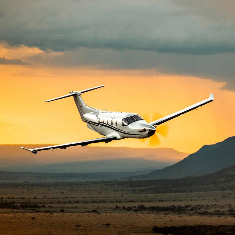 Levaero jet aircraft flying over a landscape at sunset.